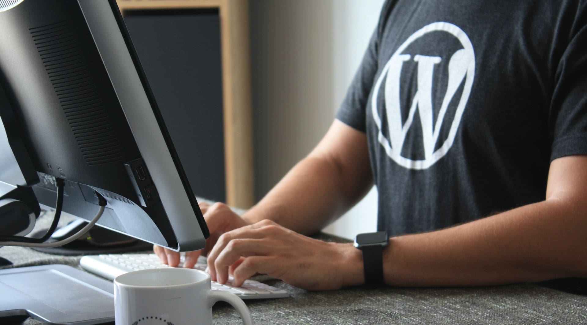 a man wearing a WordPress branded t-shirt sat in front of a computer monitor