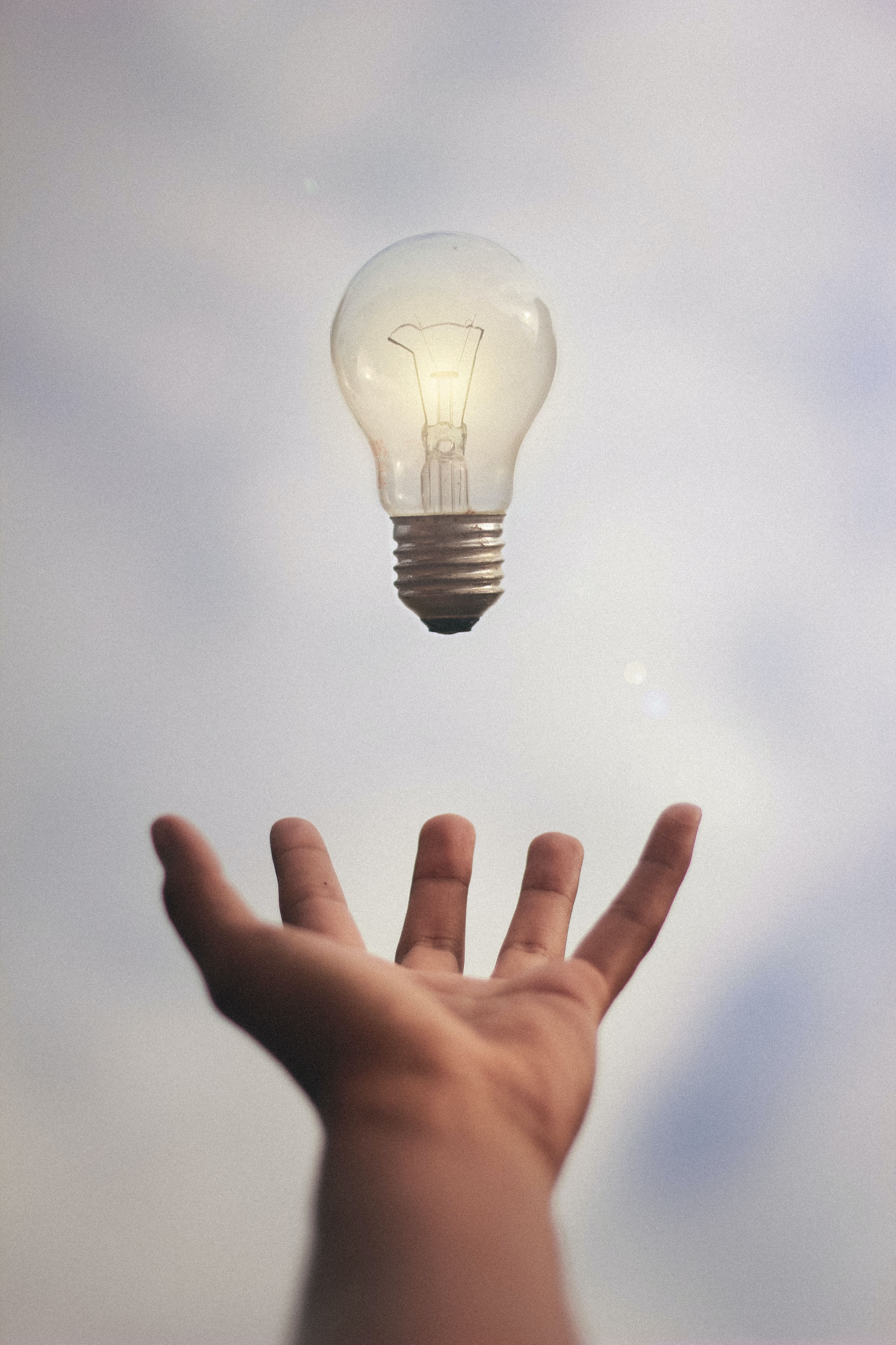 a hand outstretched with a lightbulb hovering just above it
