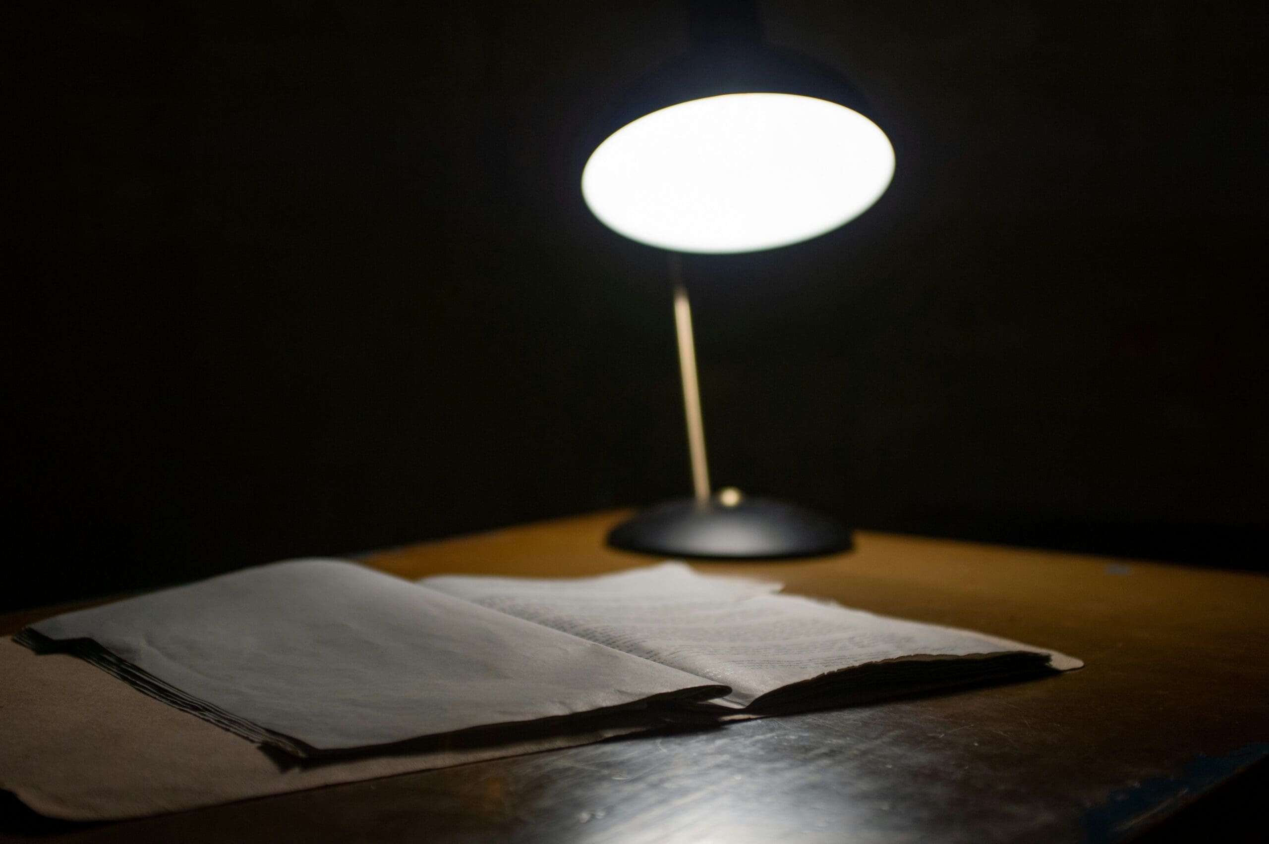 a dark room, a lamp is illuminating a few pieces of paper on a wood desk.
